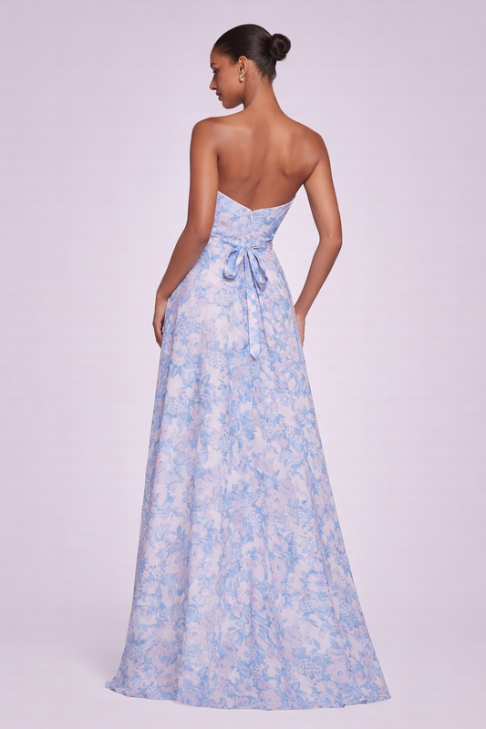  Dos d’une robe longue bustier à dos nu, avec nœud à la taille et jupe fluide à imprimé floral bleu pastel.